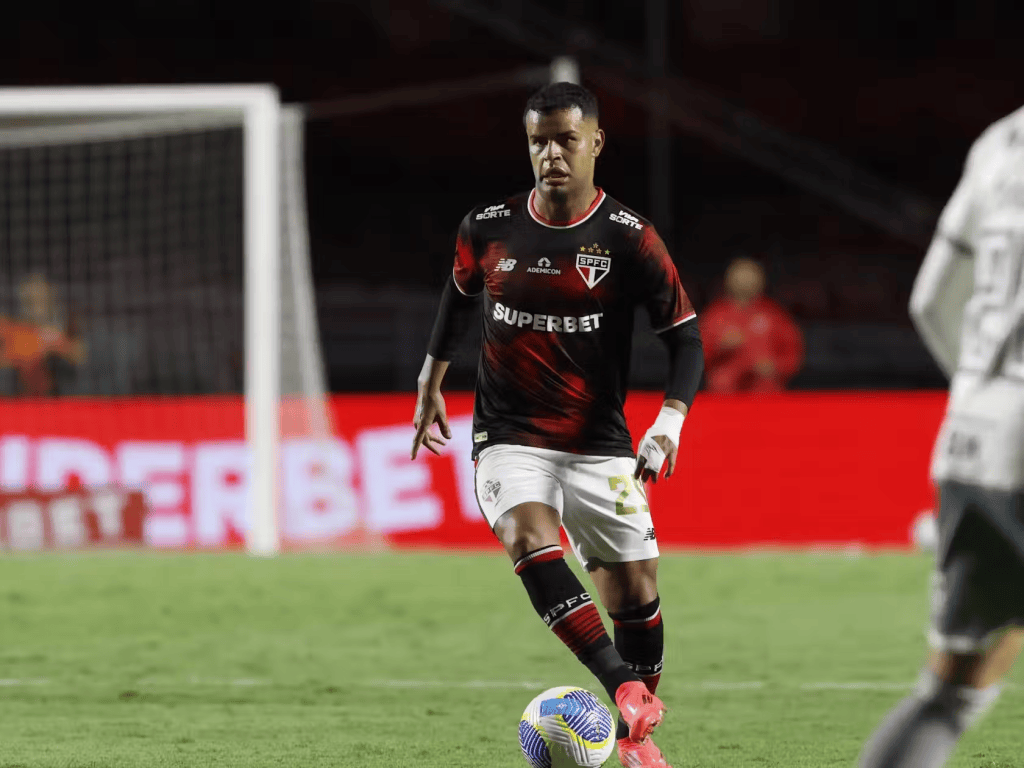 Jogador de futebol em ação, vestindo uniforme do São Paulo FC, em campo durante uma partida.