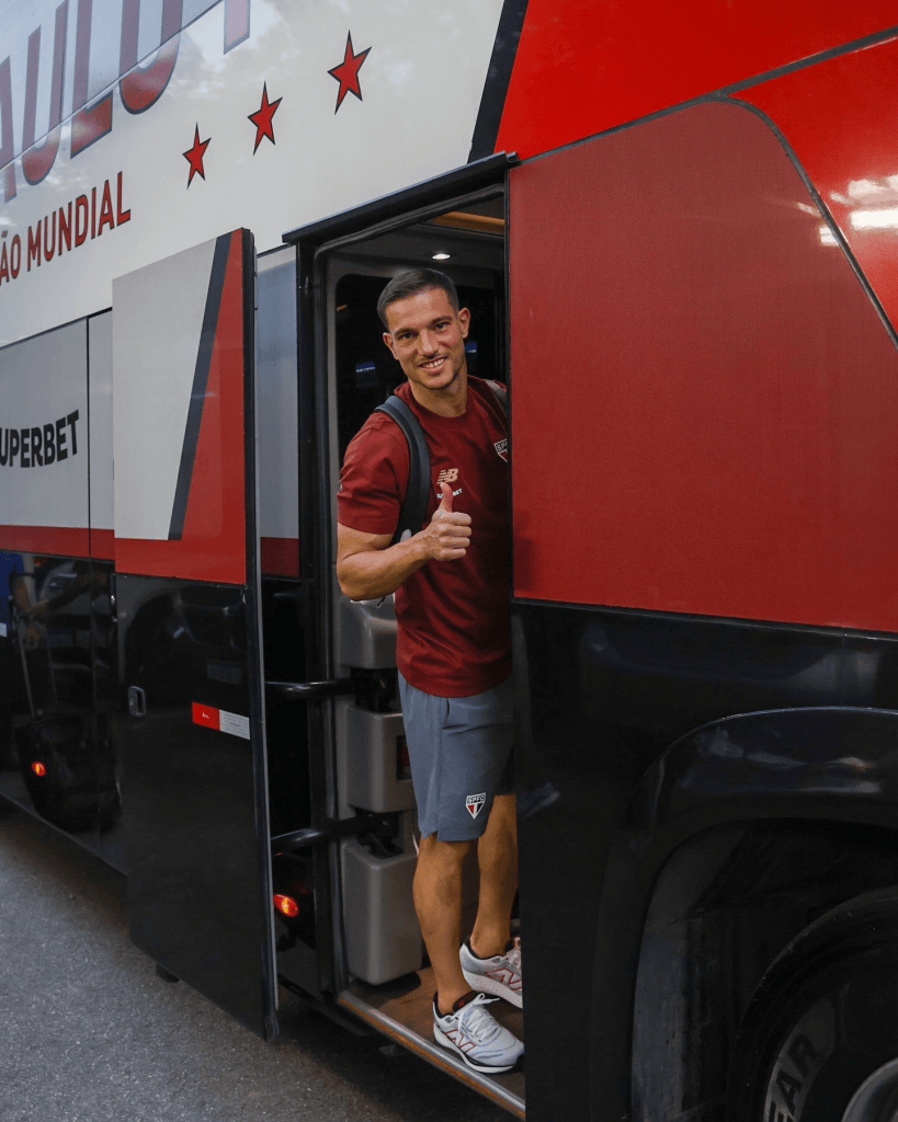 São Paulo libera lateral a procurar novo clube; agente do atleta tenta nova equipe na Europa 1 Jogador saindo de um ônibus do time, fazendo o gesto de 'joinha' com um sorriso.