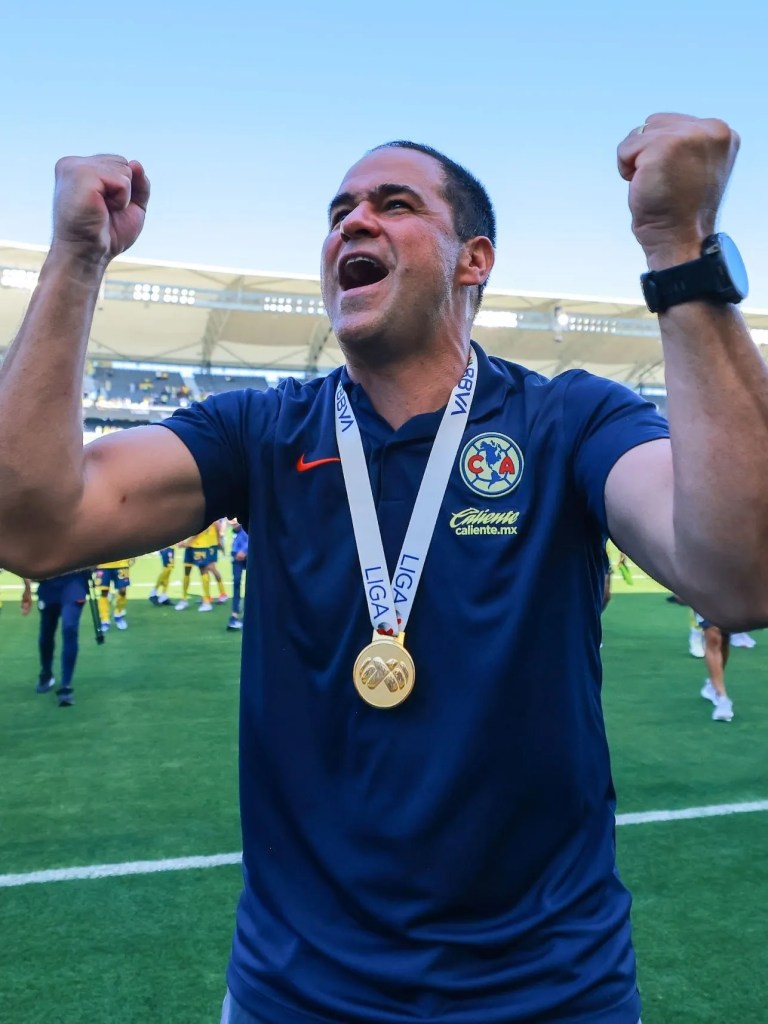 Treinador celebrando com medalha de ouro após uma vitória no futebol.