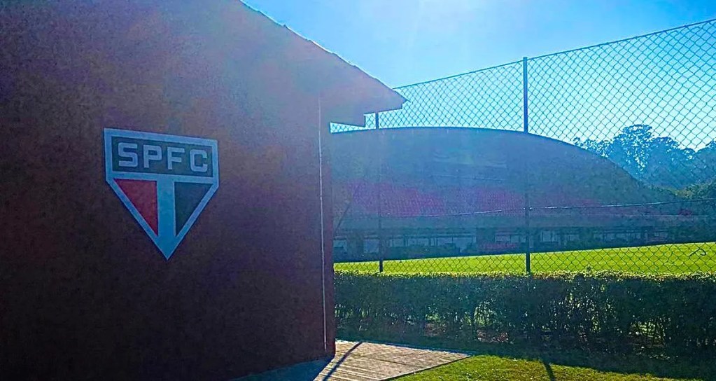 Promessa de mudanças para Cotia em 2027 no São Paulo 1 Imagem do centro de treinamento do São Paulo FC, mostrando o símbolo do clube e parte do campo coberto pela rede de proteção ao fundo.