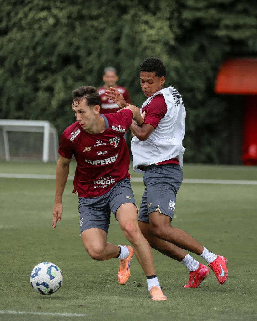 Lateral emprestado pelo São Paulo bate recorde de jogos na carreira mas tem futuro indefinido para 2027 1 Dois jogadores de futebol em um treinamento, um deles está tentando driblar o outro enquanto um terceiro jogador observa ao fundo. A cena acontece em um campo grama sob um ambiente ensolarado.