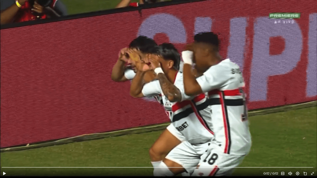 Jogadores de futebol comemorando um gol, imitando um gesto divertido em campo.