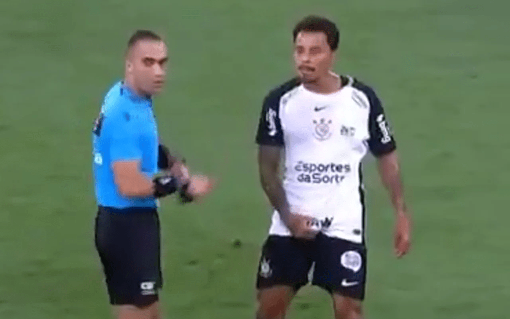 Jogador de futebol interagindo com árbitro durante uma partida.