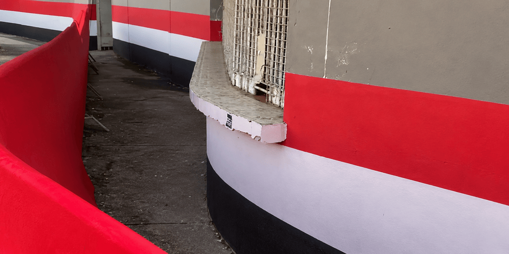 Estádio rival é pintado com cores do São Paulo e gera revolta de torcedores 1 Vista de uma parede curva com faixas vermelhas, brancas e pretas, ao lado de um cercado vermelho.
