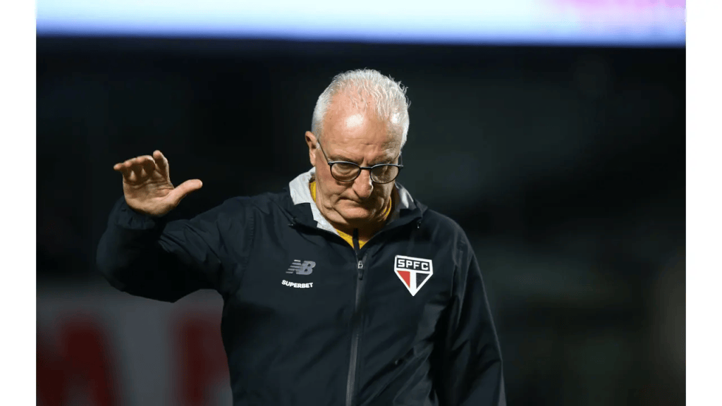 Dorival Junior quer ficar no São Paulo em 2027, afirma portal 1 Treinador de futebol em campo, vestindo jaqueta do SPFC e fazendo um gesto de despedida.